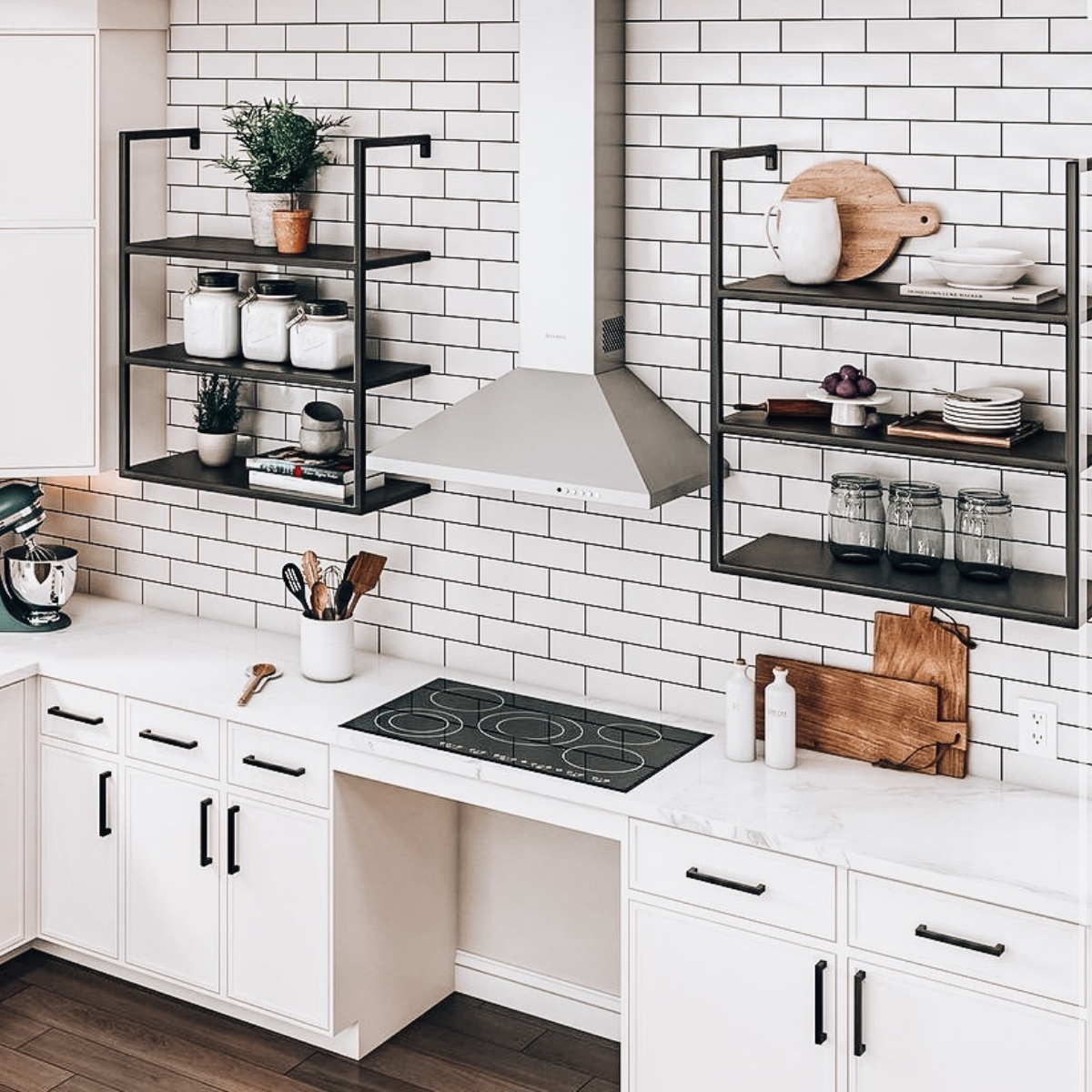 White subway tile kitchen with a stainless steel range hood, black wall-mounted shelving, and a built-in gas cooktop.
