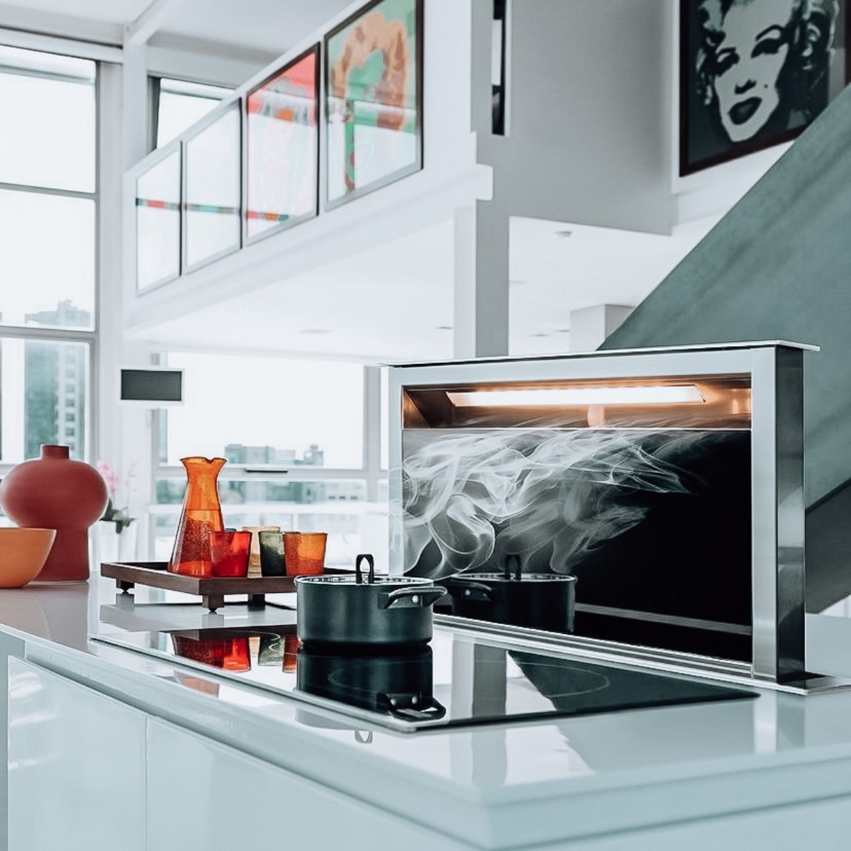 Modern pop-up downdraft range hood rising from a kitchen island, with steam visible above a pot on the cooktop.