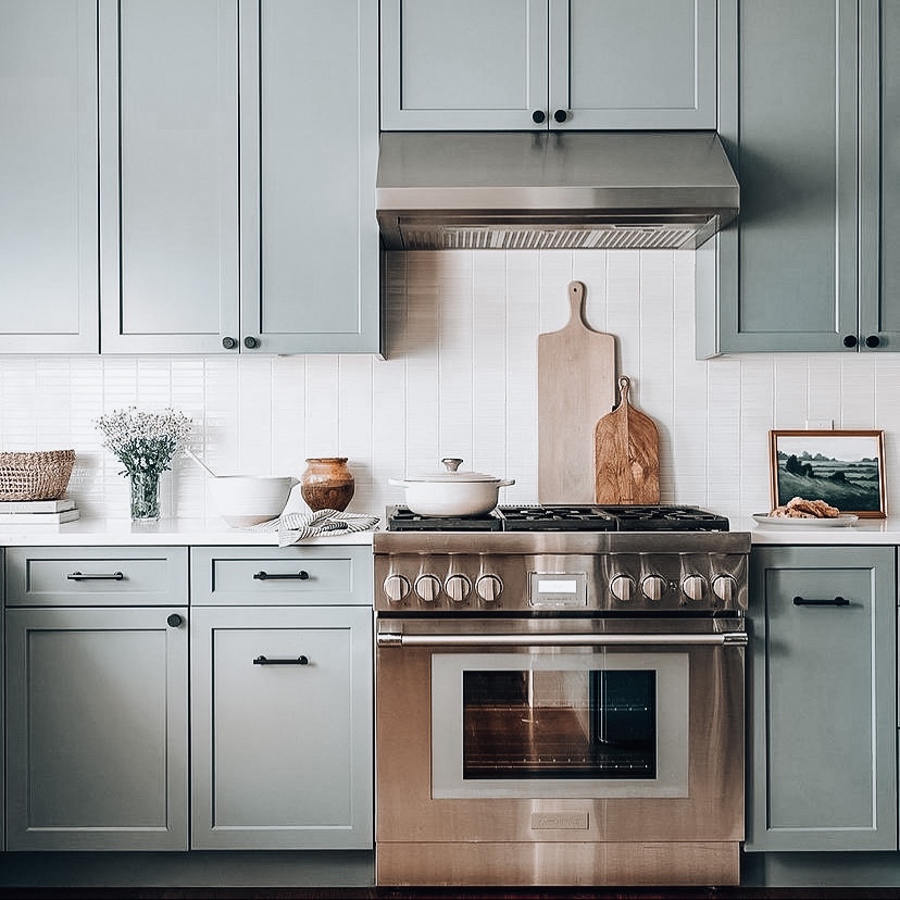 Sage green kitchen with a stainless steel range, wood cutting boards, and tile backsplash