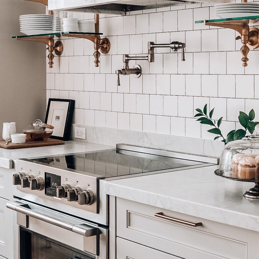 White kitchen with a stainless steel range, marble countertop, and pot filler faucet