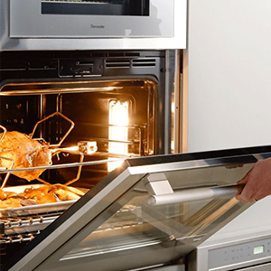 Hand opening an oven door to reveal a roasted turkey inside