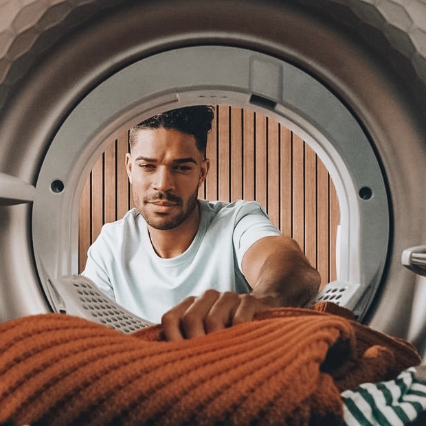 Man reaching into a front-load dryer to remove an orange knit sweater
