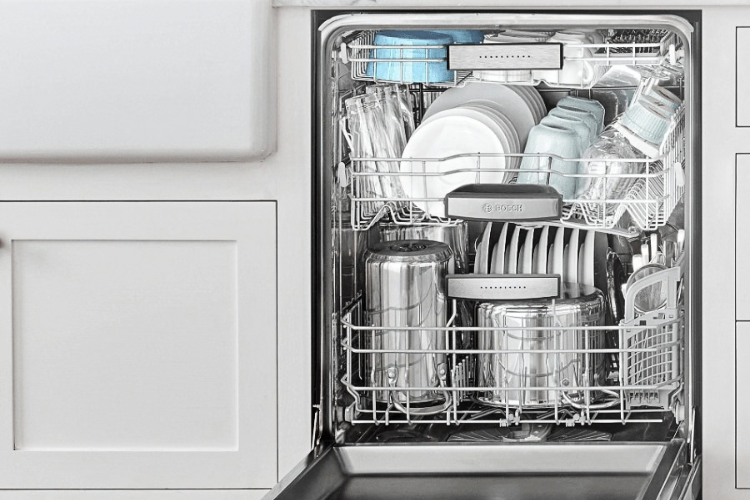 Open built-in dishwasher with two racks of plates, bowls and glasses, and stainless steel pots on the lower rack.