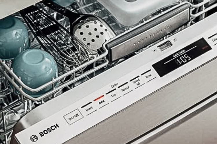 White-fronted dishwasher with a dark control strip installed under a wood countertop, with glasses and a casserole dish on top.