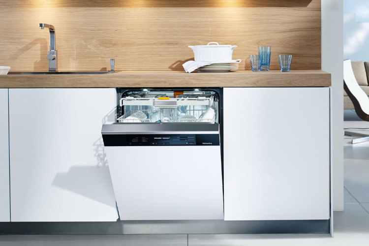 White-fronted dishwasher with a dark control strip installed under a wood countertop, with glasses and a casserole dish on top.