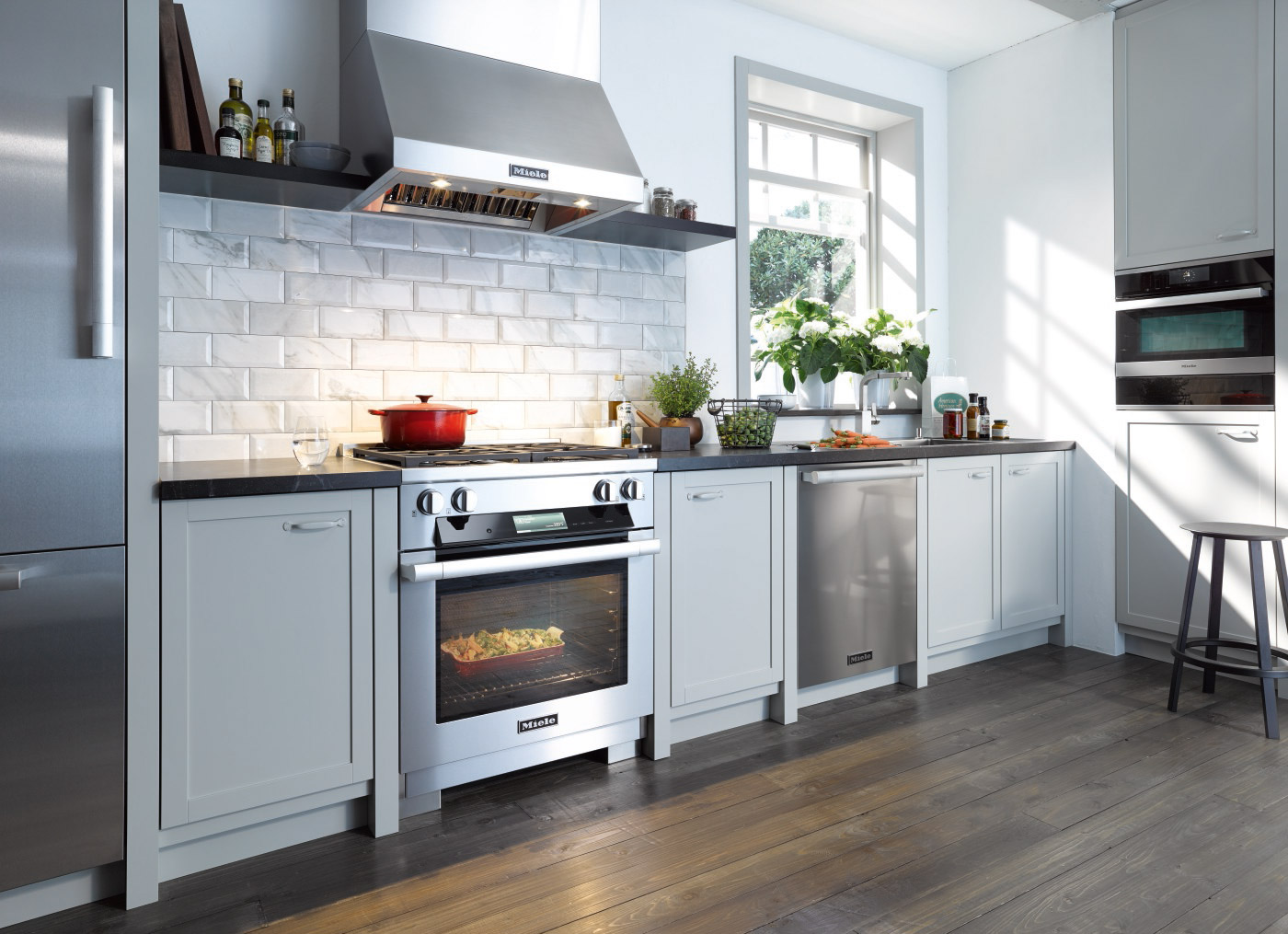 Modern kitchen with Miele stainless steel range, hood, and dishwasher set in white cabinetry.