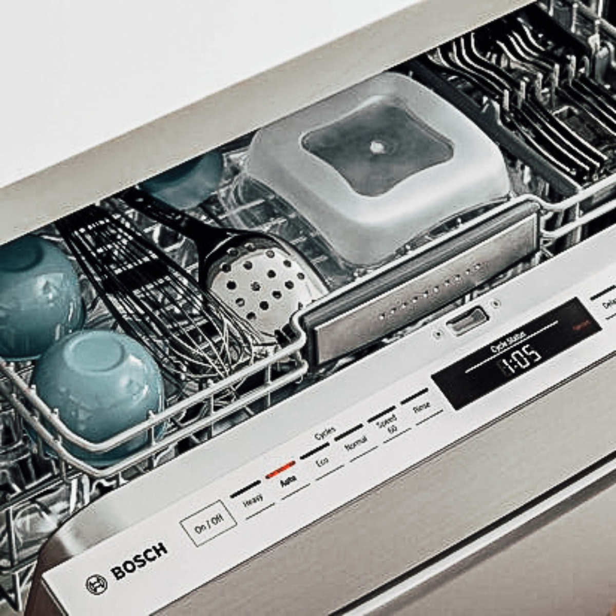 A close-up of an open Bosch stainless steel dishwasher showing a fully loaded middle rack with bowls, a container, and a basket insert, with the control panel displaying a 1:05 cycle time on Auto wash mode.
