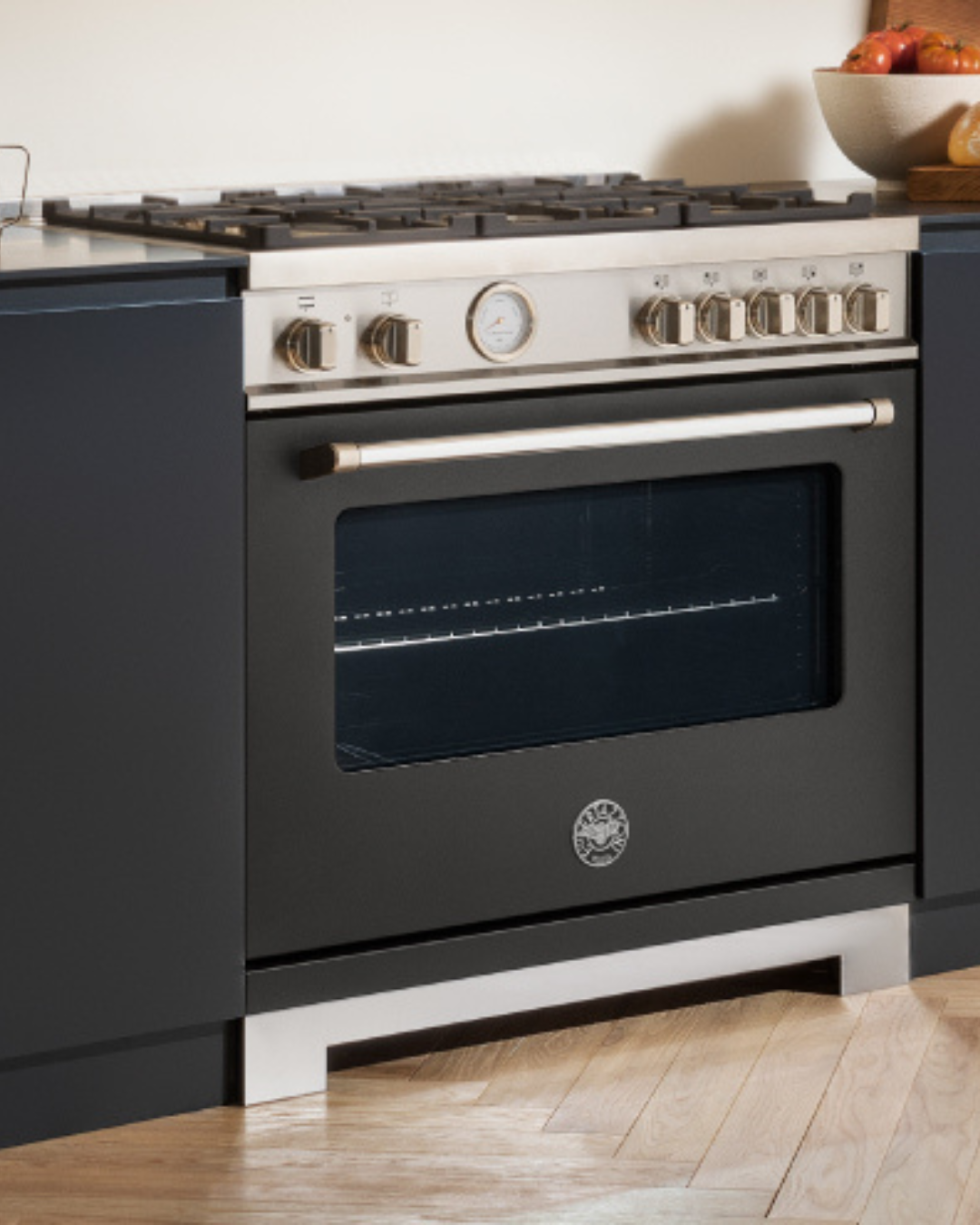 Black Bertazzoni gas range with brass-tone knobs and analog temperature gauge, built into a navy blue kitchen island
