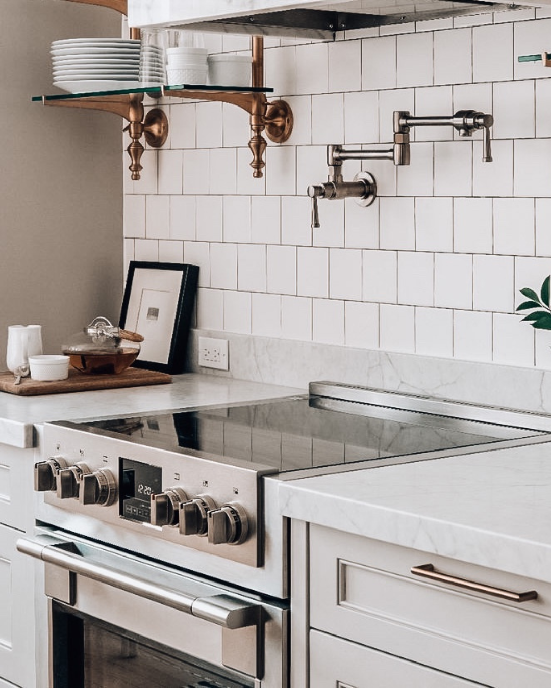 Stainless steel induction range with a wall-mounted pot filler above a white subway tile backsplash and marble countertop.
