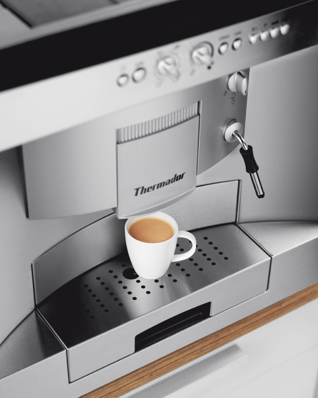 Freshly brewed espresso in a white cup sitting under the dispenser of a stainless steel Thermador built-in coffee machine.