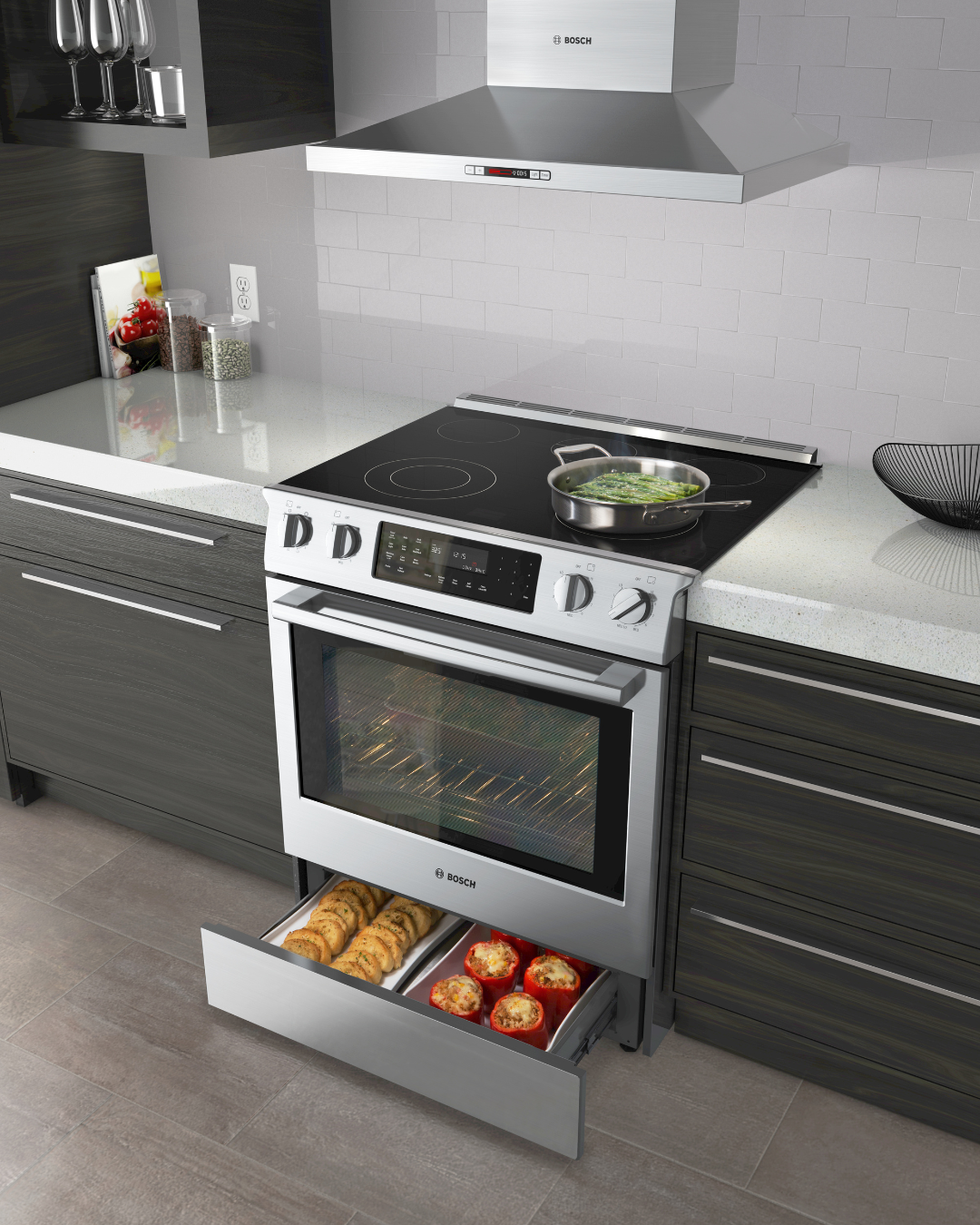 Stainless steel Bosch electric range with induction cooktop and matching wall-mounted range hood, warming drawer open with stuffed peppers and rolls.