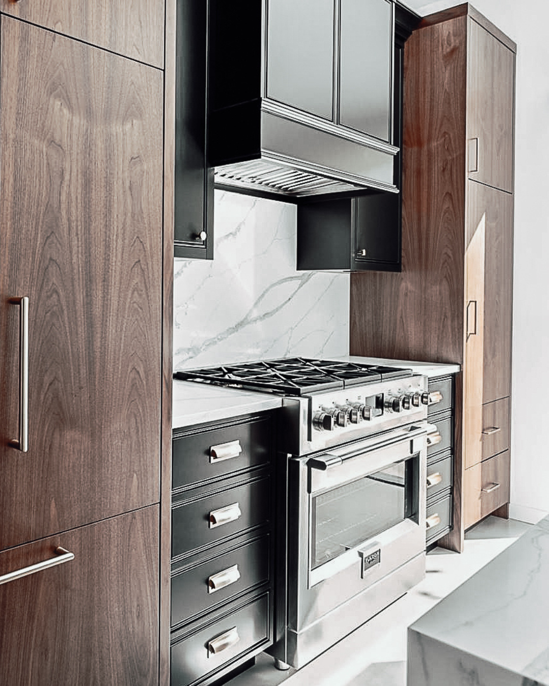 Stainless steel Bosch gas range set into dark walnut cabinetry with a marble backsplash and matching range hood.